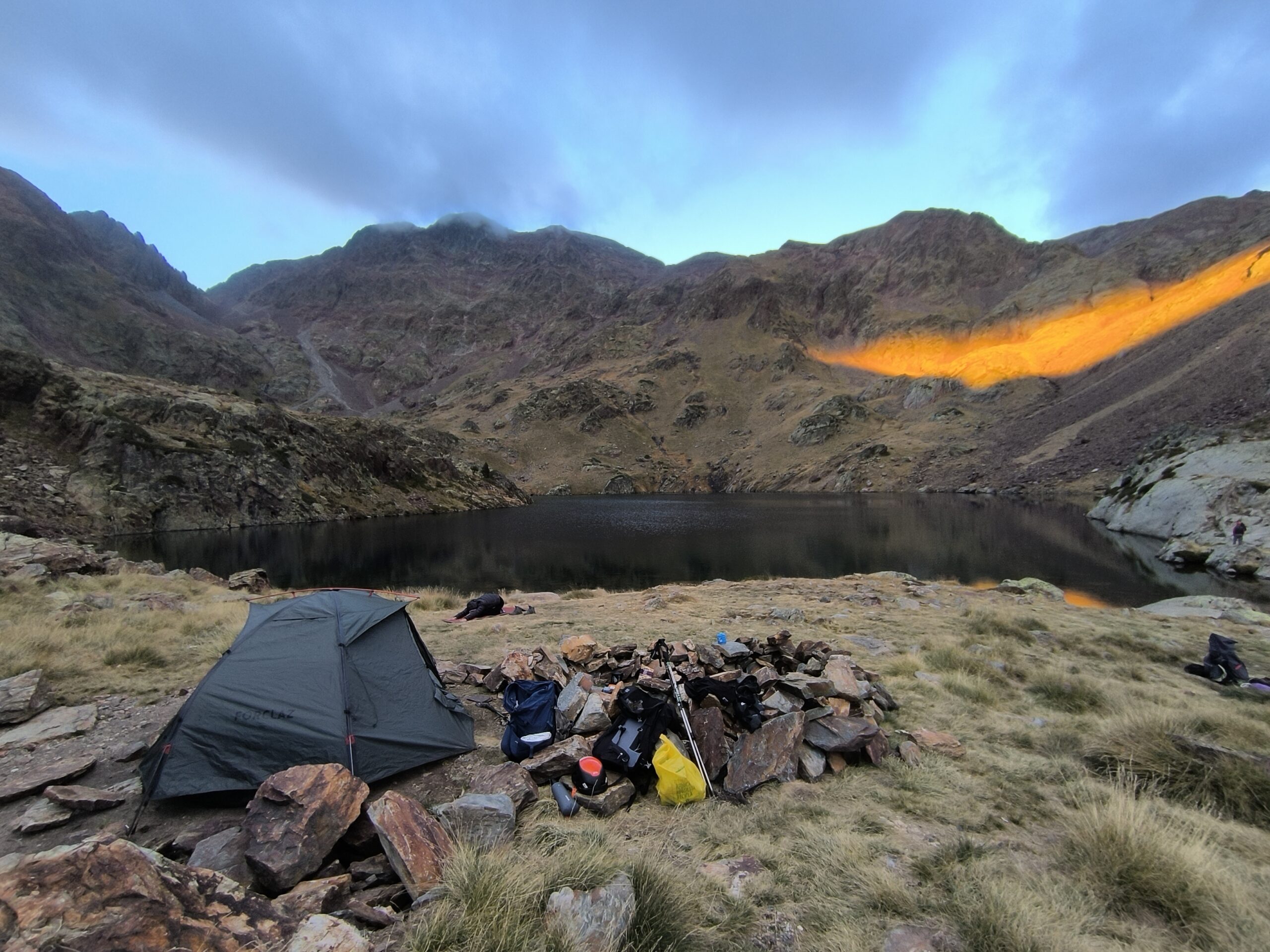 Tenda de campanya envoltada d'immenses muntanyes a la posta de sol